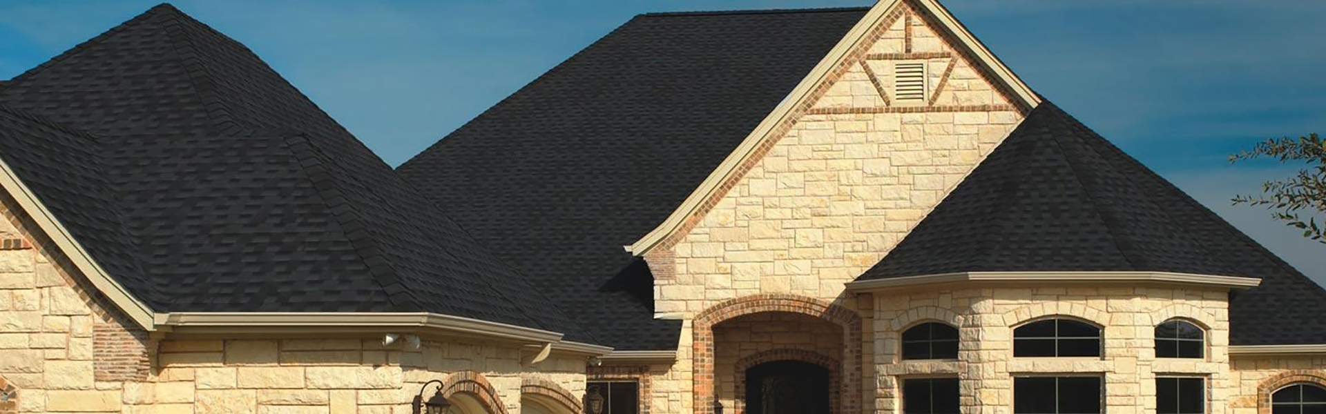 Beige stone home with a black shingle roof